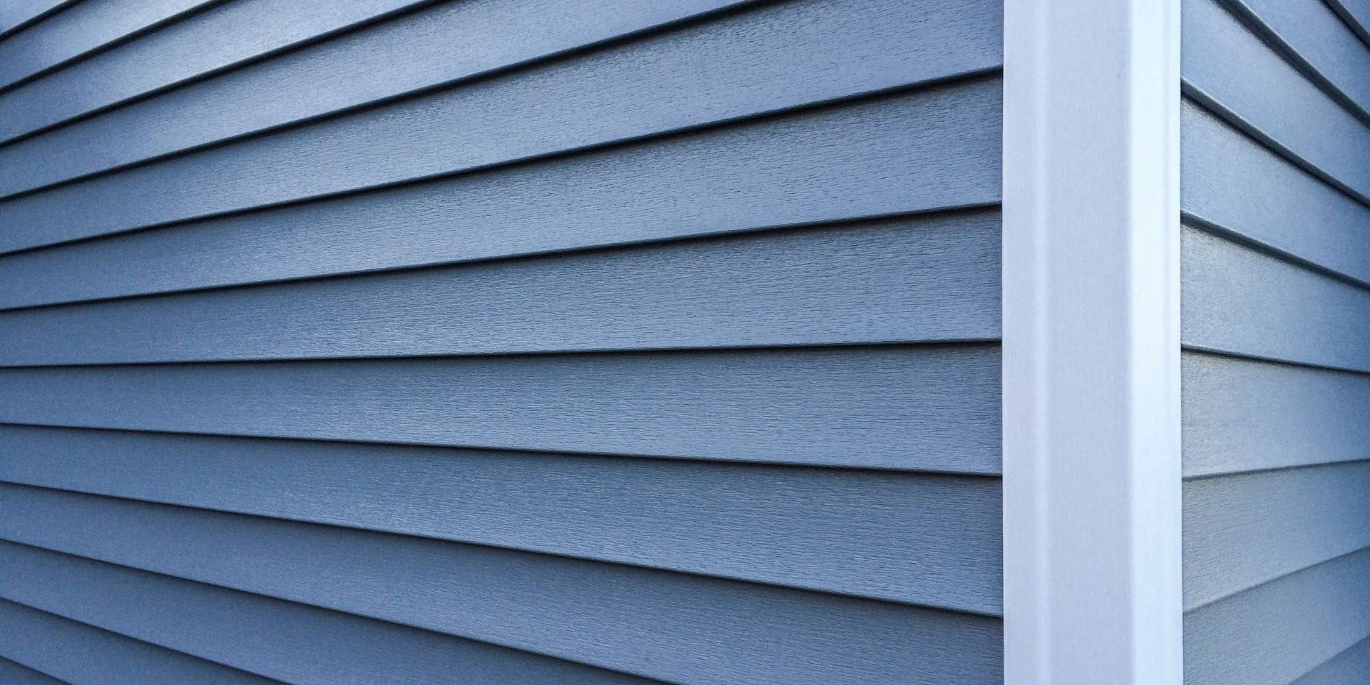 Close-up view of blue horizontal vinyl siding on a building’s corner, featuring white vertical trim—ideal inspiration for painting services Macomb & Oakland Counties, MI looking to refresh exterior finishes.
