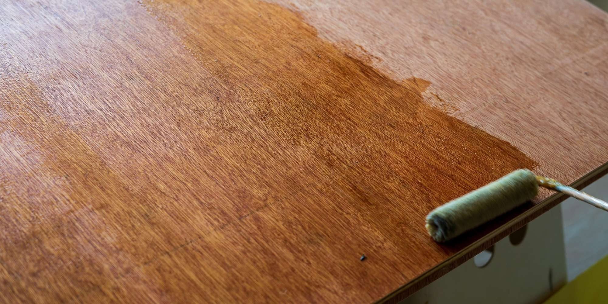 A paint roller is applying a clear varnish or sealant to a wooden surface, showcasing the skills of painting services Macomb & Oakland Counties and highlighting the contrast between treated and untreated areas.