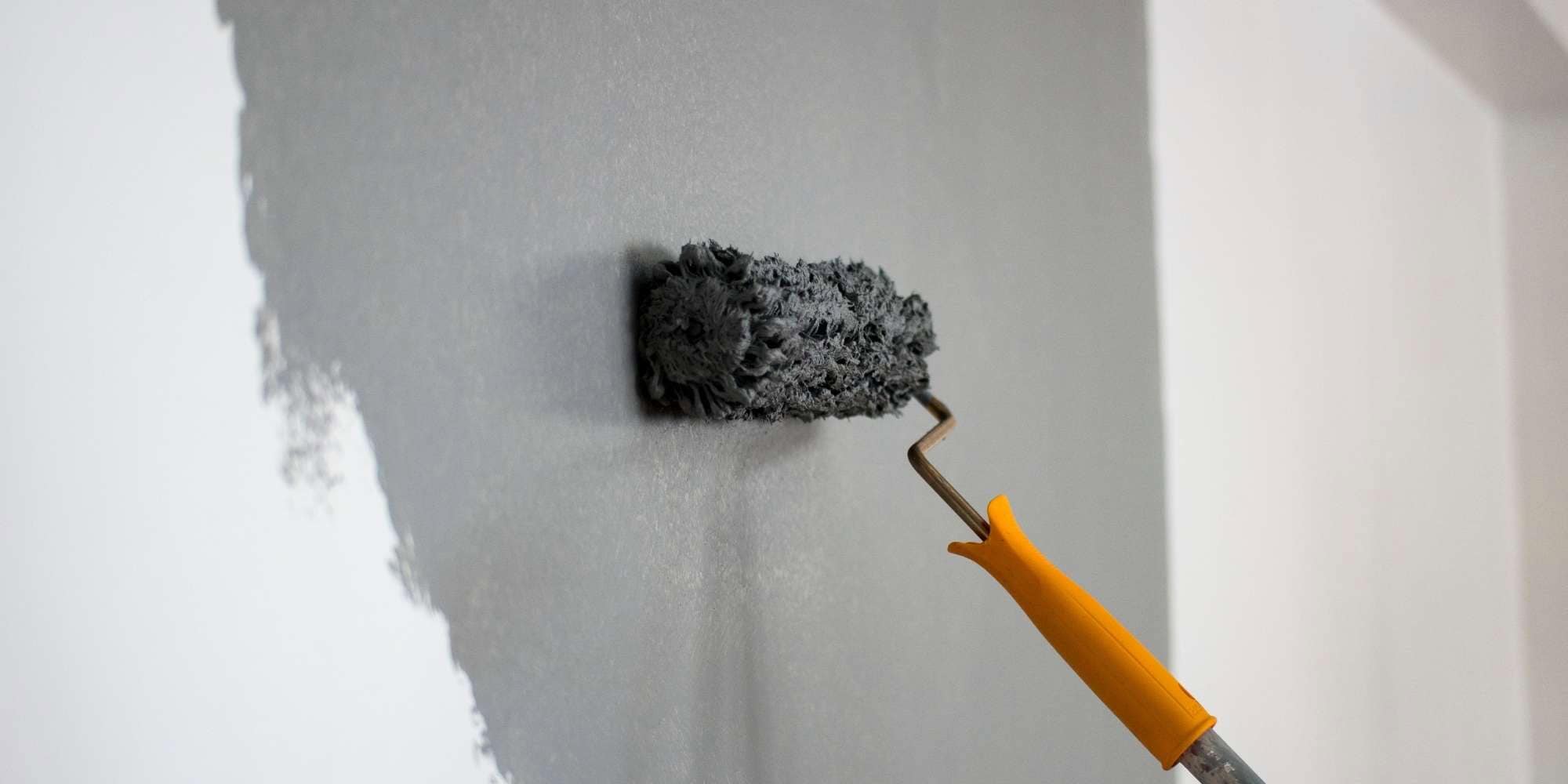 A close-up of a paint roller with a yellow handle applying gray paint on a white wall, showcasing the detailed work of Painter Macomb & Oakland Counties, MI.