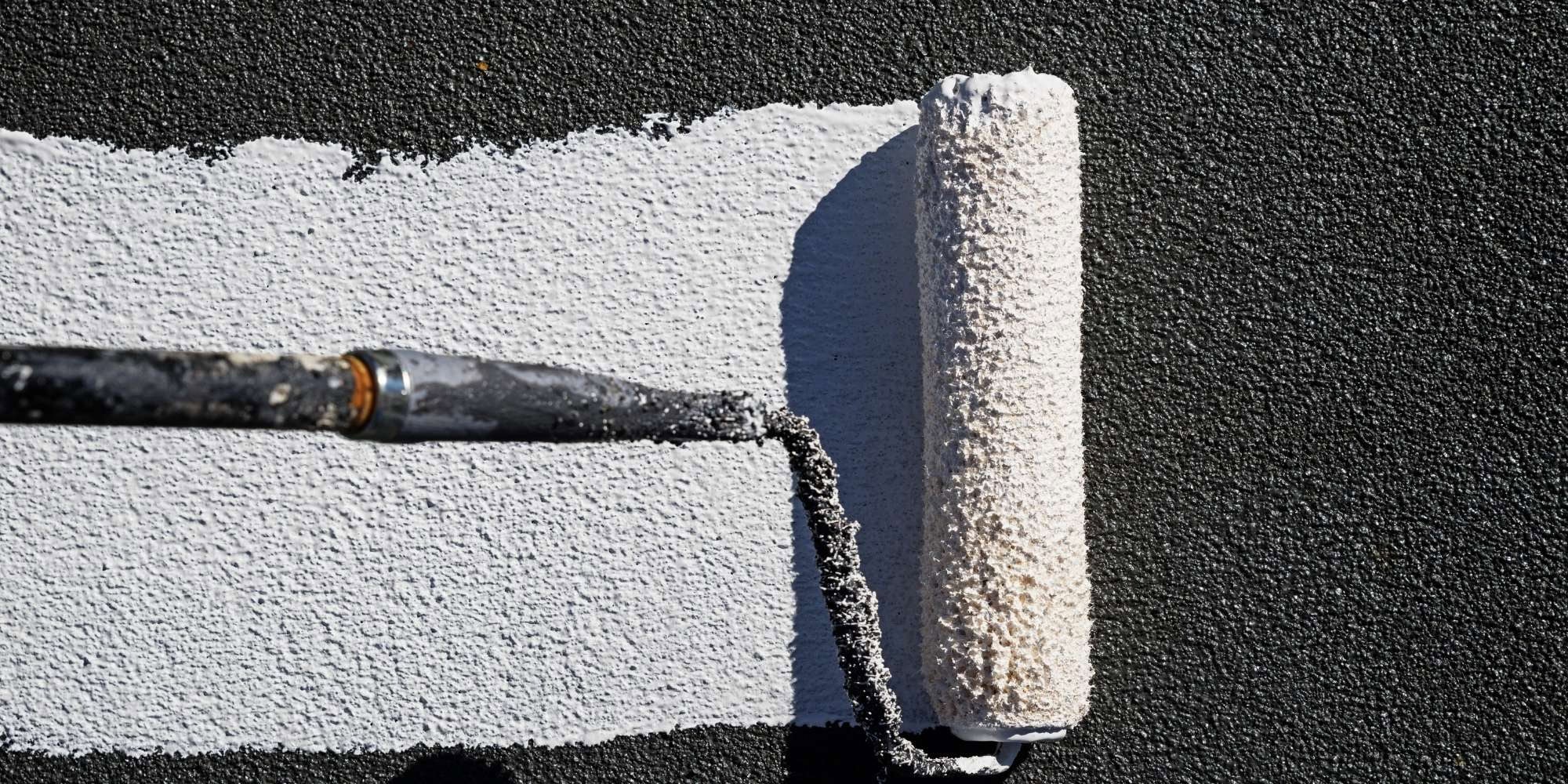 A paint roller applies a fresh coat of white paint onto a textured, dark surface, showcasing the sharp contrast achieved by professional painting services Macomb & Oakland Counties.