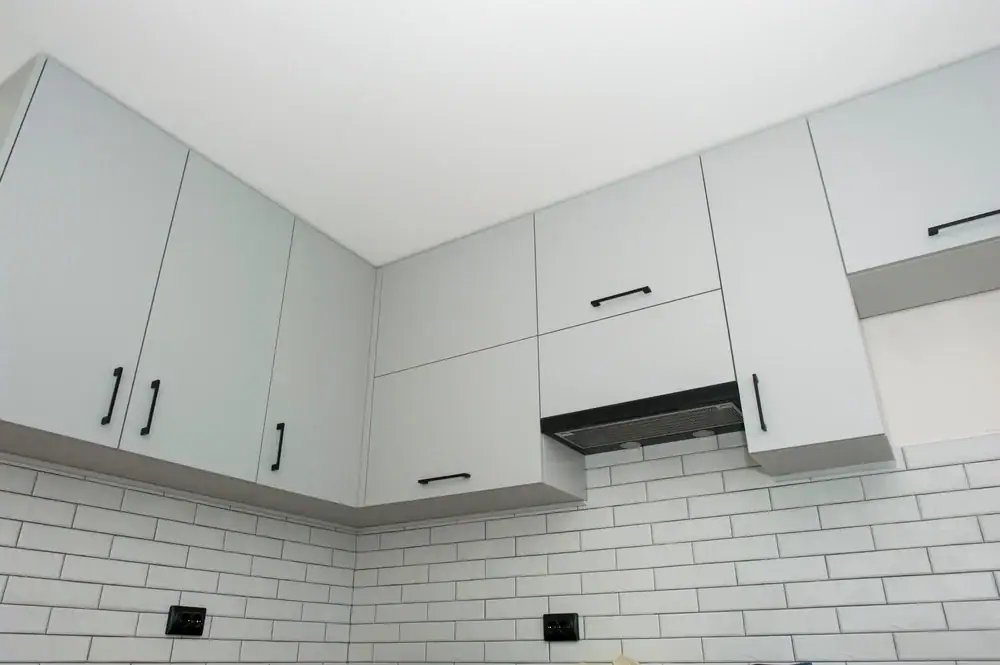 Upper kitchen cabinets with sleek, modern gray doors and black handles are mounted above a white subway tile backsplash with black grout, creating a clean, contemporary look—expertly finished by painters in Macomb & Oakland County, MI.