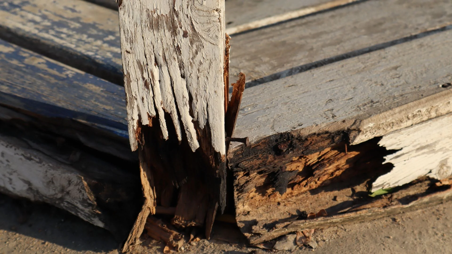 Close-up of a wooden post and boards with rot and peeling paint, showing clear structural damage.